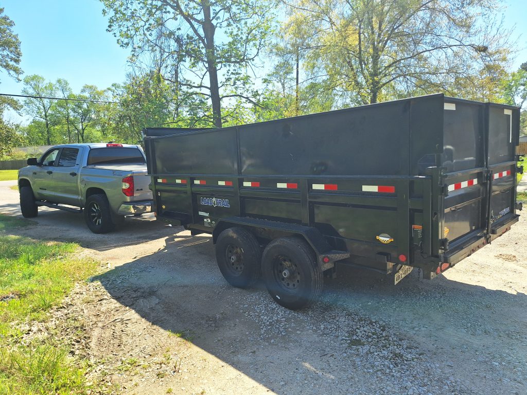 Home 1 Black Load Trail dump trailer with red and white reflective tape attached to gray pickup truck on asphalt driveway